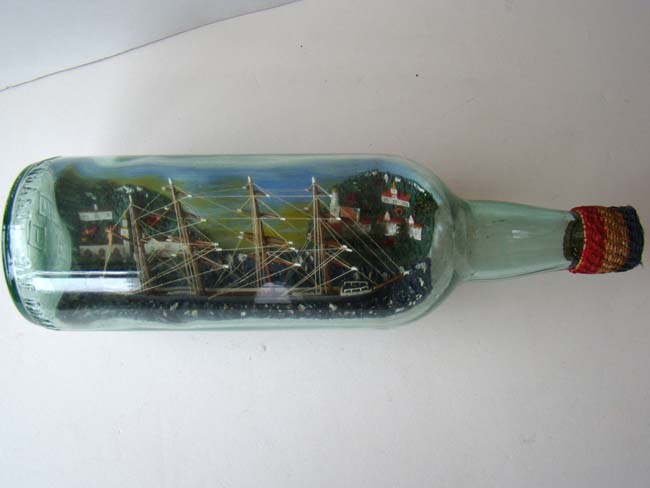 A four masted ship in a bottle flying an American flag with an American coastal town in the background. Circa 1930-1940